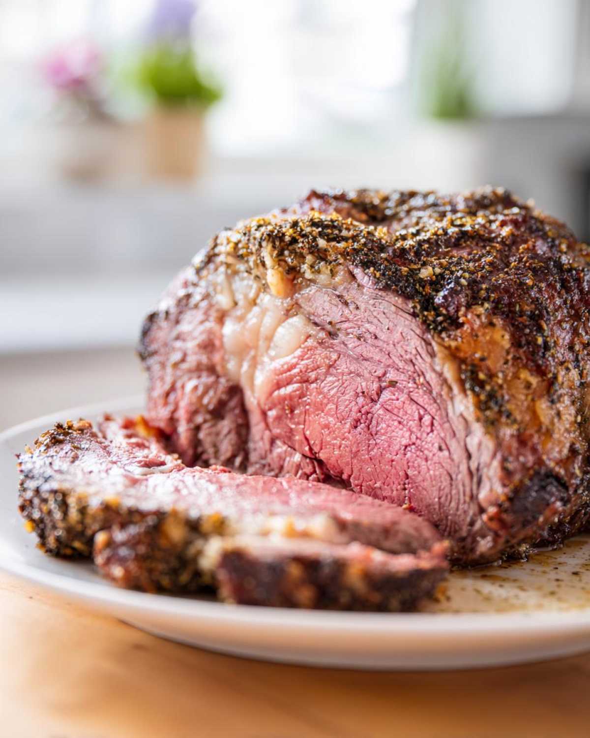 Close-up of a juicy, medium-rare rib roast, heavily seasoned and sliced on a white plate.