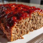 A close-up view of a thick slice of moist Keto meatloaf topped with shiny, dark red glaze.