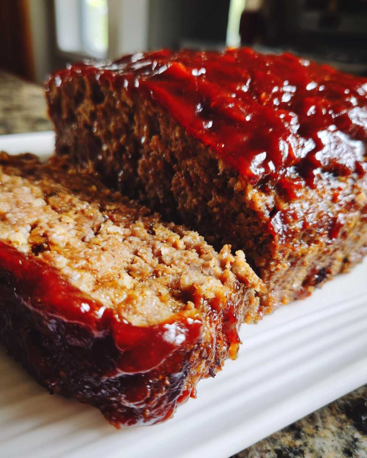 Close-up of a thick slice cut from a Keto meatloaf, covered in a shiny, dark red glaze.