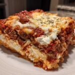 A thick, layered slice of Lasagna with Cottage Cheese on a white plate, topped with melted cheese and herbs.