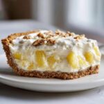 A close-up slice of million dollar pie showing a graham cracker crust, creamy filling with pineapple chunks, and a walnut topping.
