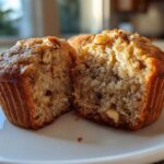 A close-up of a moist banana nut muffin cut in half, showing the fluffy interior and visible nuts.