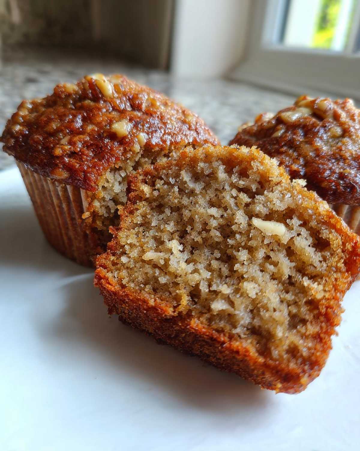 Close-up of a banana nut muffin cut in half showing the moist, textured interior and walnuts on top.