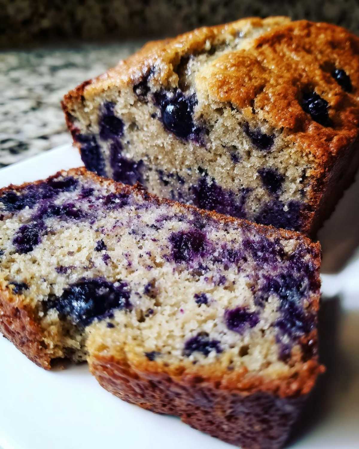 Close-up of moist blueberry banana bread loaf, showing the rich purple color of the baked blueberries throughout the crumb.
