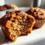 Close-up of a moist bran muffin broken in half showing the texture, with another whole bran muffin behind it.