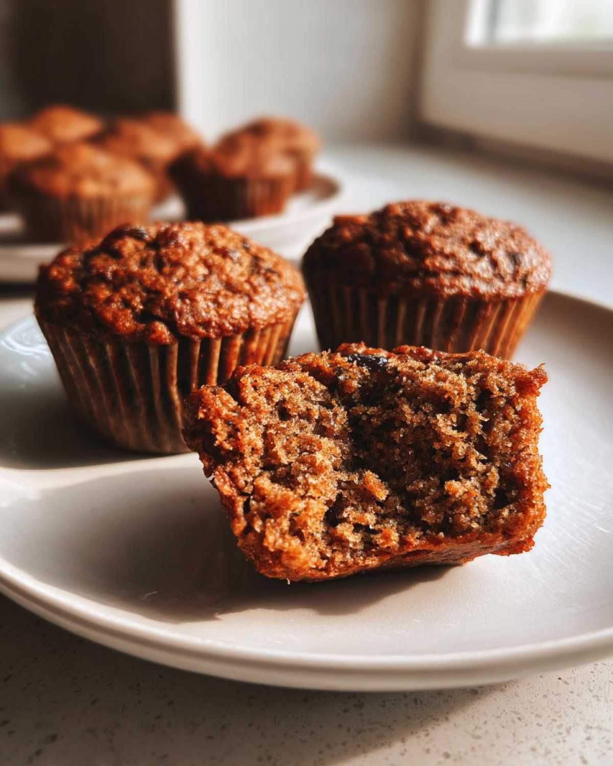 Close-up of a halved bran muffin showing its moist, textured interior next to two whole bran muffins.