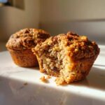 Close-up of two moist bran muffins; one is broken open showing the textured interior with raisins.