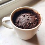 Close-up of a freshly baked, moist chocolate mug cake topped with chocolate chips inside a white mug.