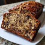 Close-up of a moist slice of date nut bread showing visible nuts and dark fruit pieces.