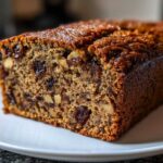 Close-up of a moist slice of date nut bread showing visible pieces of dates and walnuts throughout the crumb.