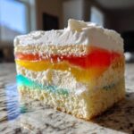 Close-up of a moist slice of 3-color jello poke cake showing layers of white cake, colorful gelatin, and whipped topping.