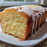 Close-up of a moist slice of lemon olive oil cake with a thick white glaze dripping down the side.