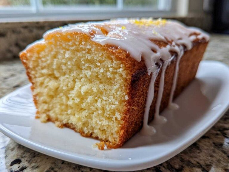 Close-up of a moist slice of lemon olive oil cake with a thick white glaze dripping down the side.