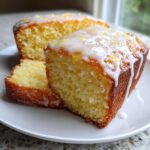 Close-up of moist olive oil cake slices topped with a thick white lemon glaze and zest.