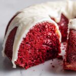 Close-up of a moist red velvet bundt cake with thick, white cream cheese frosting dripping down the sides.