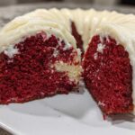 Close-up of a sliced red velvet bundt cake showing the moist, deep red interior and thick cream cheese frosting.