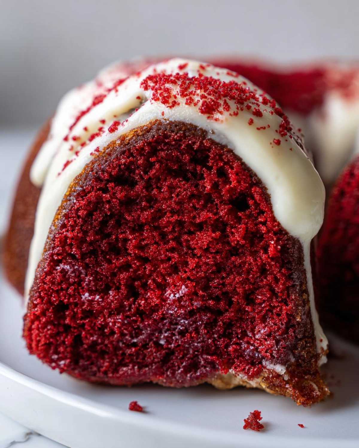 Close-up of a moist slice of red velvet bundt cake topped with cream cheese glaze and red sprinkles.