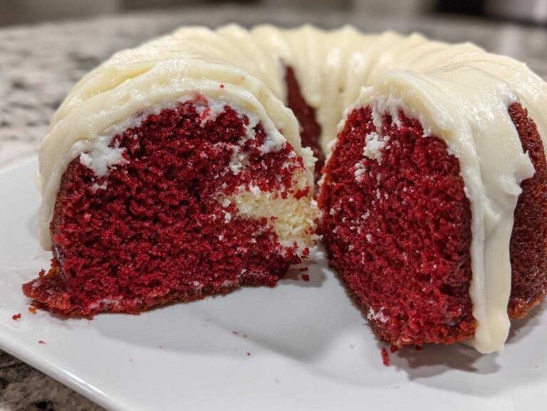 Close-up of a sliced red velvet bundt cake showing the moist, deep red interior and thick cream cheese frosting.