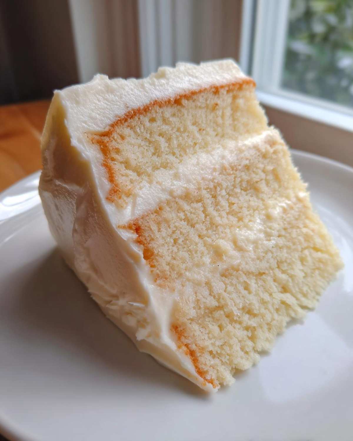 Close-up of a moist slice of two-layer vanilla cake with thick white frosting.