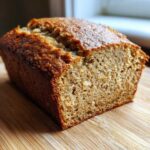 Close-up of a freshly baked loaf of moist sugar free banana bread resting on a wooden cutting board.