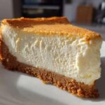 Close-up of a thick slice of creamy new york cheesecake with a golden baked top and graham cracker crust.