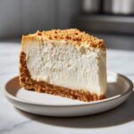 A thick, creamy slice of new york cheesecake with a graham cracker crust and crumb topping on a small plate.