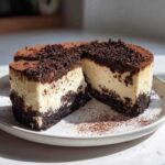 A slice of creamy no bake tiramisu cheesecake with a dark chocolate crust and topping.