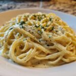 Close-up of spaghetti coated in creamy Olive Garden Alfredo Sauce, topped with black pepper and parsley.