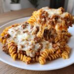 A serving of cheesy pizza pasta with rotini noodles and meat sauce, showing a large cheese pull as it is lifted.