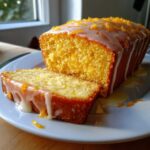 Close-up of a sliced orange juice cake loaf topped with white glaze and zest.