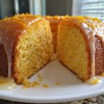 A slice cut from a moist orange juice cake, topped with a thick citrus glaze and zest.