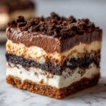 A decadent, layered square slice of Oreo Dirt Cake showing chocolate pudding, cream cheese layers, and cookie crumbs.