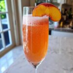 A vibrant, bubbly peach bellini recipe served in a champagne flute, garnished with a fresh peach slice.