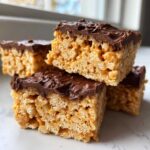 Close-up of stacked peanut butter rice krispie treats topped with melted chocolate frosting.