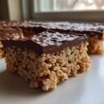 Close-up of a thick peanut butter rice krispie treats bar topped with glossy melted chocolate.