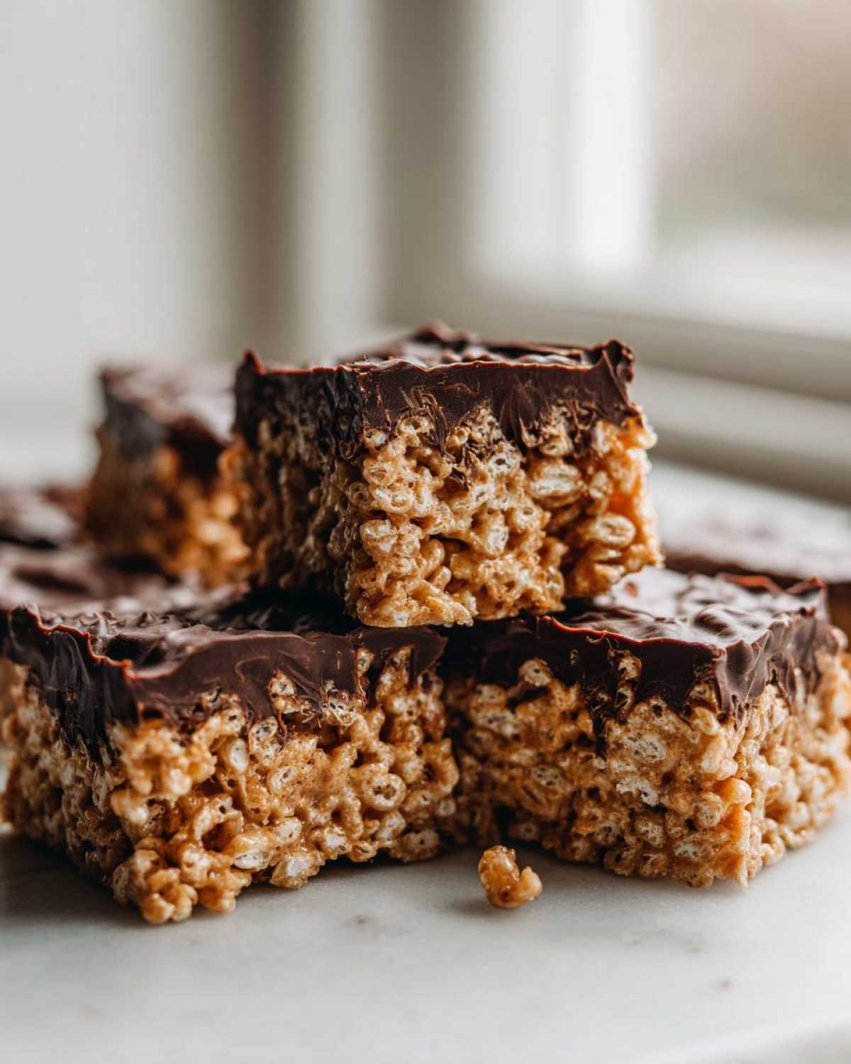 Close-up of stacked peanut butter rice krispie treats topped with a thick layer of melted chocolate.