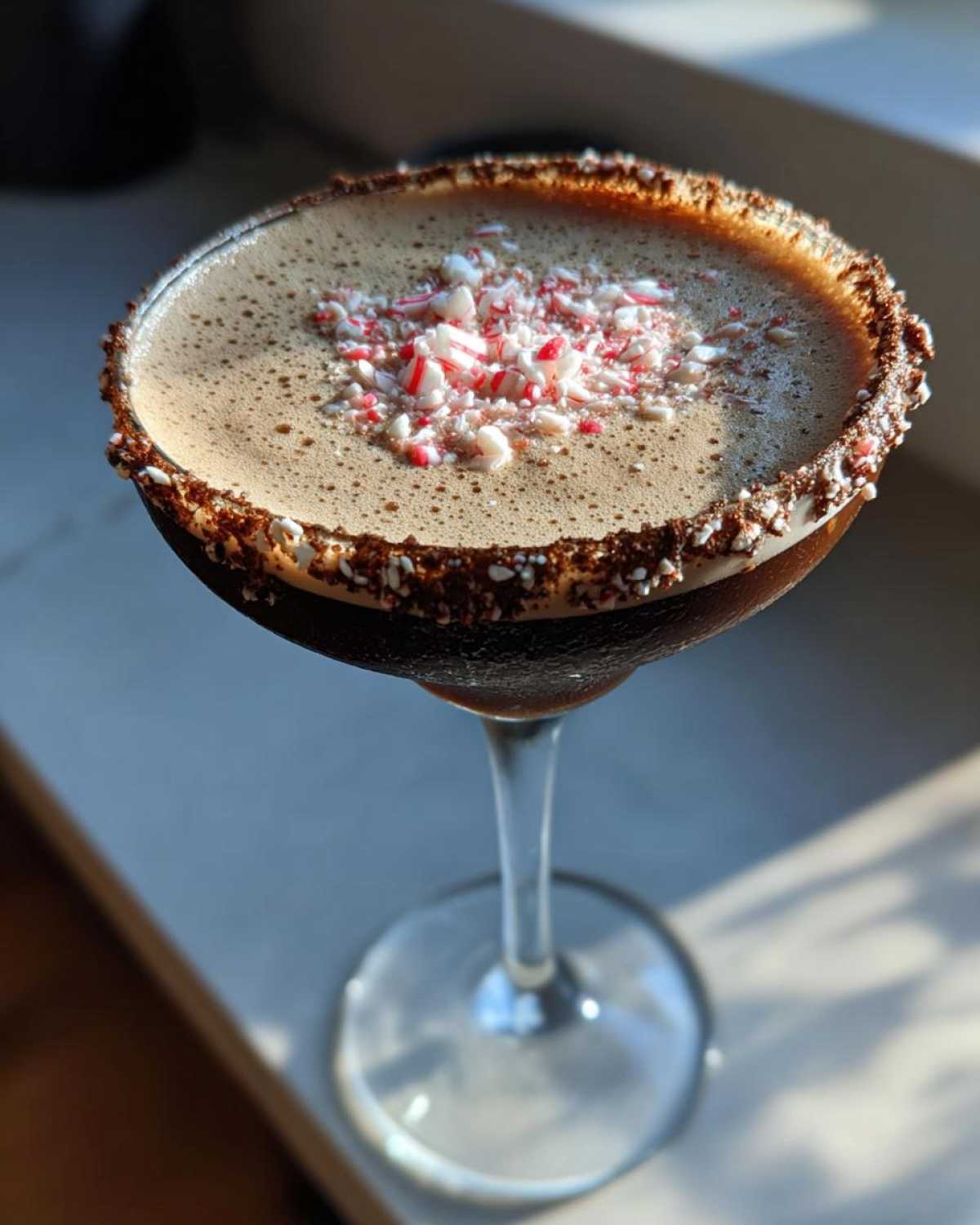 A rich, dark peppermint espresso martini garnished with crushed candy canes and a chocolate rim.