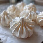 Close-up of several perfectly piped, white meringue cookies resting on crumpled parchment paper.
