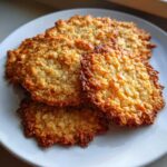 A stack of golden brown, lacy oatmeal lace cookies piled on a white plate, showing their crisp texture.