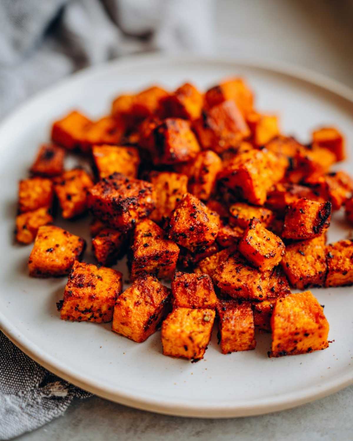 A close-up of perfectly seasoned and caramelized roasted sweet potato cubes piled on a light plate.