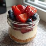 A single serving Protein Cheesecake layered in a small glass jar, topped with fresh strawberries and blueberries.