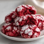 A stack of vibrant red velvet cake mix cookies dusted heavily with powdered sugar, one cookie is broken open.
