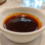 Close-up of thick, dark homemade teriyaki sauce with visible spice flecks in a small white bowl.
