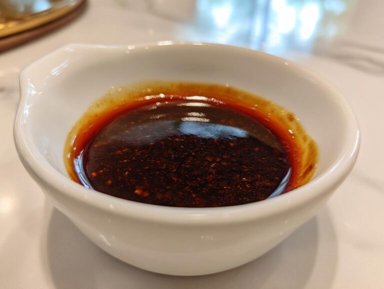 Close-up of thick, dark homemade teriyaki sauce with visible spice flecks in a small white bowl.