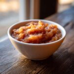 Close-up of chunky, homemade applesauce spiced with cinnamon served in a small white bowl on dark wood.