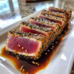 Five slices of perfectly seared ahi tuna, crusted in sesame seeds, resting in soy sauce.