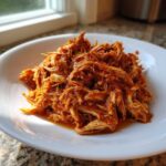 Close-up of rich, saucy shredded chicken tinga piled high on a white plate.