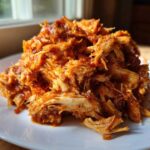 Close-up of a mound of saucy, shredded chicken tinga piled high on a white plate.