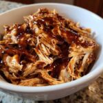 Close-up of shredded crockpot teriyaki chicken generously drizzled with thick teriyaki sauce in a white bowl.