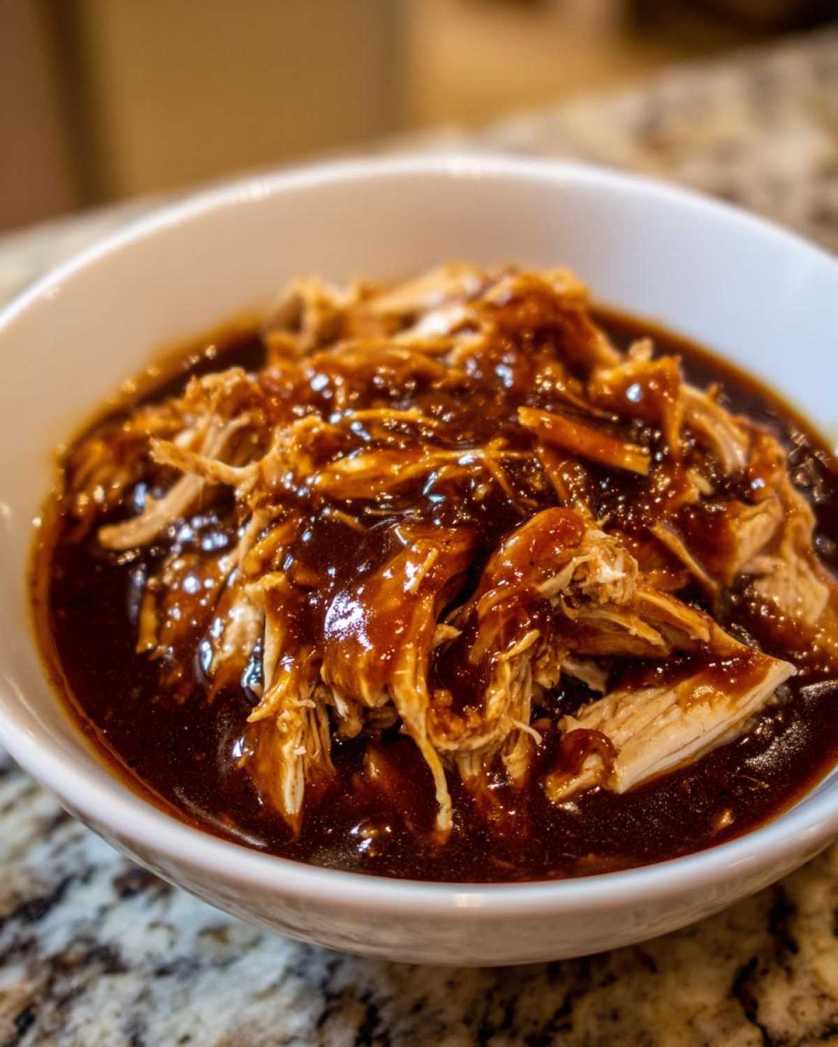 Close-up of shredded crockpot teriyaki chicken generously coated in a thick, dark teriyaki sauce in a white bowl.
